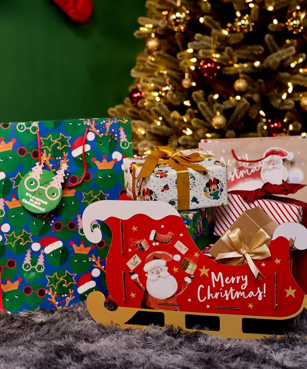 Christmas gift bags, wrapped presents and a festive Santa sleigh gift set displayed in front of a decorated Christmas tree. Christmas gift bags, wrapped presents and a festive Santa sleigh gift set displayed in front of a decorated Christmas tree.